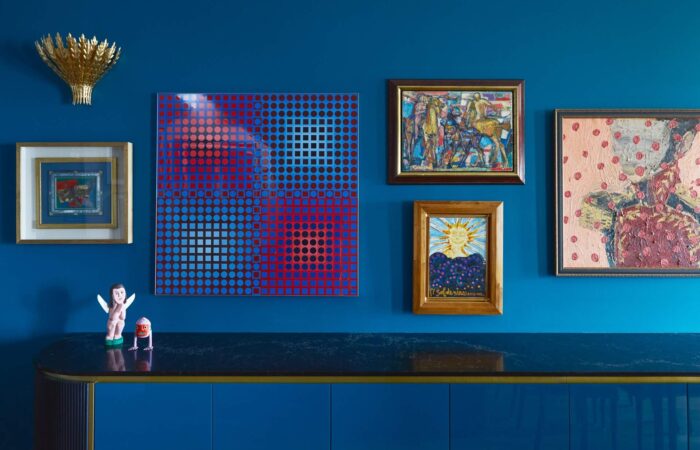 A modern interior showcasing a blue wall adorned with various artworks, including a prominent dotted pattern piece in red and blue, framed pictures, and decorative figurines.