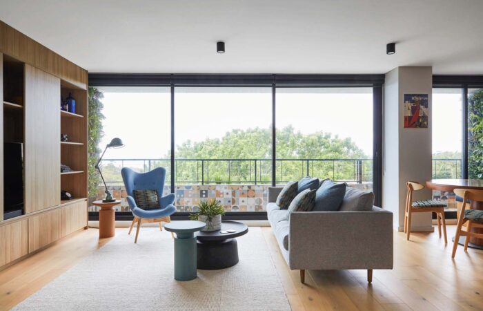 A modern living room featuring large windows with greenery outside, a stylish blue chair, a cozy gray sofa, and contemporary furniture pieces. Ideal for interior design inspiration.