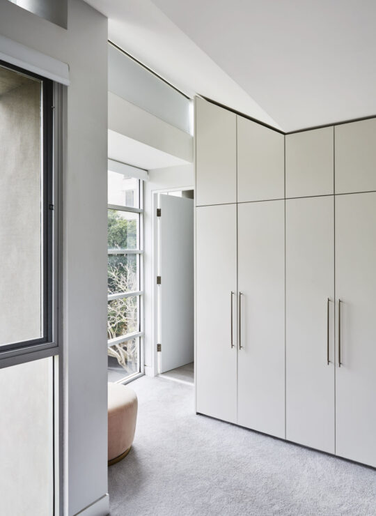 Modern bedroom interior featuring a sleek white closet, large windows, and a minimalist design, perfect for creating a spacious and inviting atmosphere.